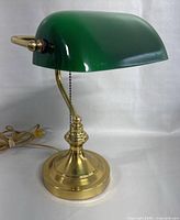 Side view of the desk lamp showing green glass shade and brass base with cord and pull chain.
