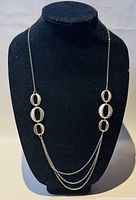 Silver necklace displayed on black bust, showing overall length and design with oval links.
