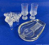 Four glass items: Kosta Boda candle holder, two Iittala shot glasses, Holophane dish against blue background.