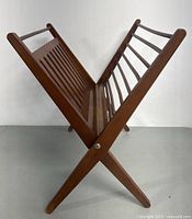 Side angled view of teak folding magazine holder showing the slatted design and folding legs.