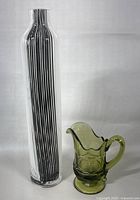 The two glass items on a neutral gray background showing the striped tall vase and the green creamer side by side for size reference.
