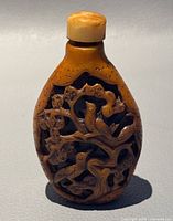 Front view of the small brown hand carved bottle with birds on branches motif.