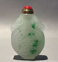 Front view of the old Asian hand carved jade perfume/snuff bottle showing floral carvings and green patches.