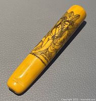 Hand decorated Asian pipe showing one side with a seated figure in traditional clothing and leaves.