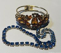 Image of the amber rhinestone bangle bracelet with blue rhinestone necklace beside it on a white background.