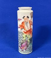 Front view of 4.5 inch tall cylindrical porcelain vase with hand painted elderly figure and dragon design on white background against blue fabric.