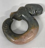 Front angled view of the jade ornament showing the curled shape, facial and claw details, and part of the engraved signature.