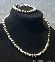 Necklace and bracelet displayed on black bust showing overall design with round silver-tone beads.