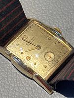 Close-up showing the front of the vintage Gruen watch with gold filled rectangular case and striped fabric strap.