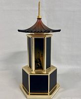 Front view of octagonal gold-tone metal music box with black enamel panels and pagoda-style roof