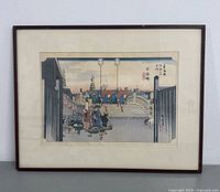 Framed woodblock print showing people crossing a bridge in a traditional Japanese setting.