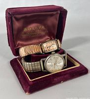 Both watches in a vintage burgundy velvet case showing the Bulova logo inside lid, watch face details, and bands.