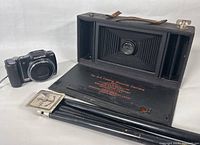Vintage Kodak Number 3-A Folding Brownie Camera open showing lens, bellows, and front panel text alongside Olympus SZ-10 digital camera.