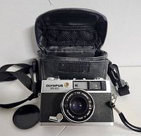 Front view of Olympus 35 ED film camera with lens cap off and black carrying case open showing interior mesh pocket