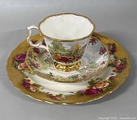 Full view of Royal Albert teacup, saucer, and 7 inch side plate with floral and scenic garden designs, gold accents
