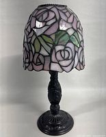Front angle view of Tiffany style stained glass candle holder with pink rose pattern and black ornate base.