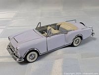 Front three-quarter view of lavender die-cast convertible showing grille, bumper, missing windshield, and whitewall tires