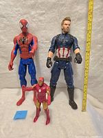 All three Marvel superhero action figures: Spider-Man, Captain America, Iron Man displayed standing against a white background with a measuring tape showing size of Spider-Man and Captain America figures at about 12 inches tall.
