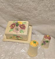 Butter dish with lid and floral handle, showing hand-painted flowers on textured cream ceramic, sitting on a rectangular base.