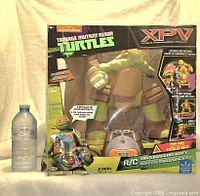 Front view of unopened boxed Micelangelo R/C Skateboarding Mikey toy with water bottle for scale.