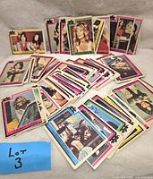 Photo shows a spread of approximately 44 colorful collectible cards with vintage TV and movie characters, arranged fanned out and stacked on a flat surface with a blue sticky note labeled Lot 3.