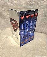 Metallic box set containing four VHS tapes of the Superman movie series, showing the spines labeled Superman, Superman II, Superman III, Superman IV.