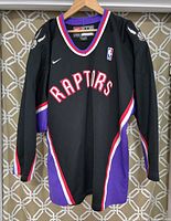 Front of men's black Toronto Raptors NBA warm-up jersey with Raptors logo and Nike swoosh.