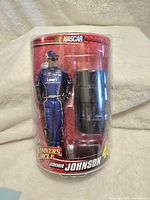 Front view of new Jimmie Johnson figure in Lowe's suit inside clear blister pack with red Winners Circle NASCAR branding and black accessory beside figure.