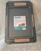 Photo of 3 new sealed metal cookie sheets stacked with product label visible on top sheet.
