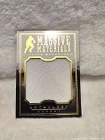 Front of the card showing Massive Materials white jersey swatch with black and gold trim around the card.