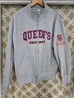 Full front view of grey zip jacket with Queens University embroidered text and front pockets