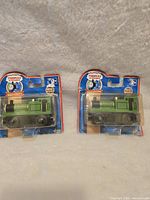 Photo showing two Thomas & Friends wooden trains "Smudger" in original packaging with some visible wear and repairs to cardboard.