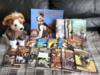 Full view of all lot items showing 16 books, calendar, and plush dog toy arranged on plaid surface