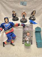 Lot of toy collectibles including Buddy L hockey doll in St. Louis Blues uniform, Marvel figurines under domes, Brett Hull bobblehead, blue toy car, and small blue metal scoreboard toy.