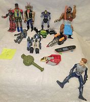 Multiple vintage collectible toys displayed on a white cloth, including Biker Mice, MOTU, Transformers and other action figures with one note 'Lot 4'