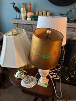 Image showing two table lamps on a wooden table with white hexagonal shade and gold cylindrical shade with a white base