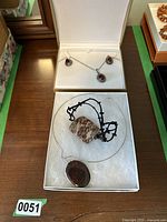 Two stone pendant necklaces displayed in white jewelry boxes on a wooden surface.