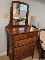 Front view of the antique dresser showing the wood grain, five drawers with metal handles, and the attached swivel mirror.