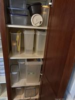 Shelf holding multiple tall and medium size clear plastic food storage containers including cereal containers with flip and snap lids.