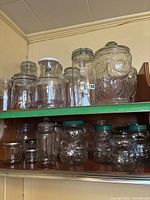 Overall view of upper and lower shelves showing various glass jars including the owl cookie jar, tall mason jars, and Kraft peanut butter bear-shaped jars.