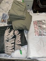 Microfibre bedding sheets, wool blanket, and mattress protector shown folded and stacked on mattress.