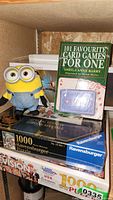 Shelf with brand new Ravensburger puzzles, card game book, card decks, and Minion plush