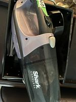 Photo showing Shark cordless handheld vacuum cleaner inside a black box with charging dock visible underneath