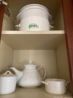White ceramic casseroles including one with lid and handles on a cupboard shelf