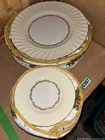 Eight plates stacked, showing both large and small sizes. Plates have cream color with a gold rim and floral border pattern.