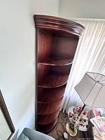 Full view of the solid wood corner shelf showing its tall, curved design placed in a corner.