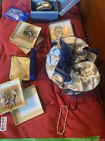 Photo of multiple costume jewelry pieces including brooches in boxes, a bracelet, and a blue satin pouch on a red surface