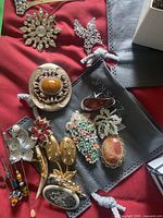 Selection of brooches and hairpins laid out on a red fabric, showing various ornate designs with rhinestones, faux pearls, enamel, and metalwork.