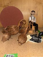 Photo showing the three woven wicker bird figurines, the painted wooden seated man figurine, and the painted wooden loon bird figurine.
