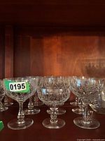 Front view of several cut crystal dessert glasses with etched patterns, arranged in two rows on a wooden shelf.
